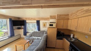 Ett kompakt kök med träskåp, en mikrovågsugn, ett handfat och ett fönster med gardiner.