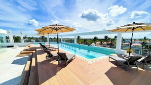 Una piscina sul tetto con lettini e ombrelloni, circondata da un solarium in legno e un cielo sereno.