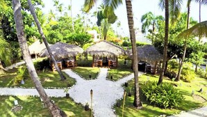Una località turistica tropicale con capanne a tetto di paglia, palme e un viale centrale.