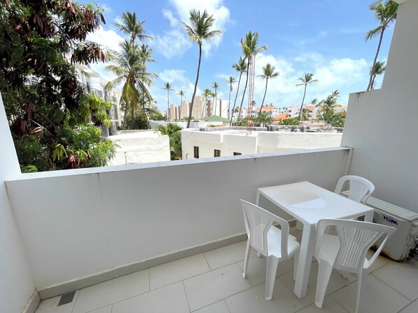 A balcony with a white table and chairs, overlooking a cityscape with palm trees and buildings. - CARIBBEAN DUCASSI Tropicana HOTEL (Punta Cana)