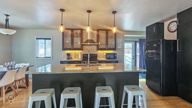 A modern kitchen with a central island, bar stools, pendant lighting, and a refrigerator.