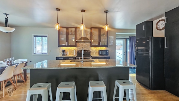 A modern kitchen with a central island, bar stools, pendant lighting, and a refrigerator.