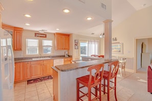 A spacious kitchen with wooden cabinets, a granite countertop, and a central island with bar stools. - JL #899 - Casa Dianey - Oceanside - Private Pool - Hot tub - SSCA Amenities (Southern Shores)