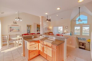 A spacious kitchen with granite countertops, wooden cabinets, and a dining area with red chairs. - JL #899 - Casa Dianey - Oceanside - Private Pool - Hot tub - SSCA Amenities (Southern Shores)