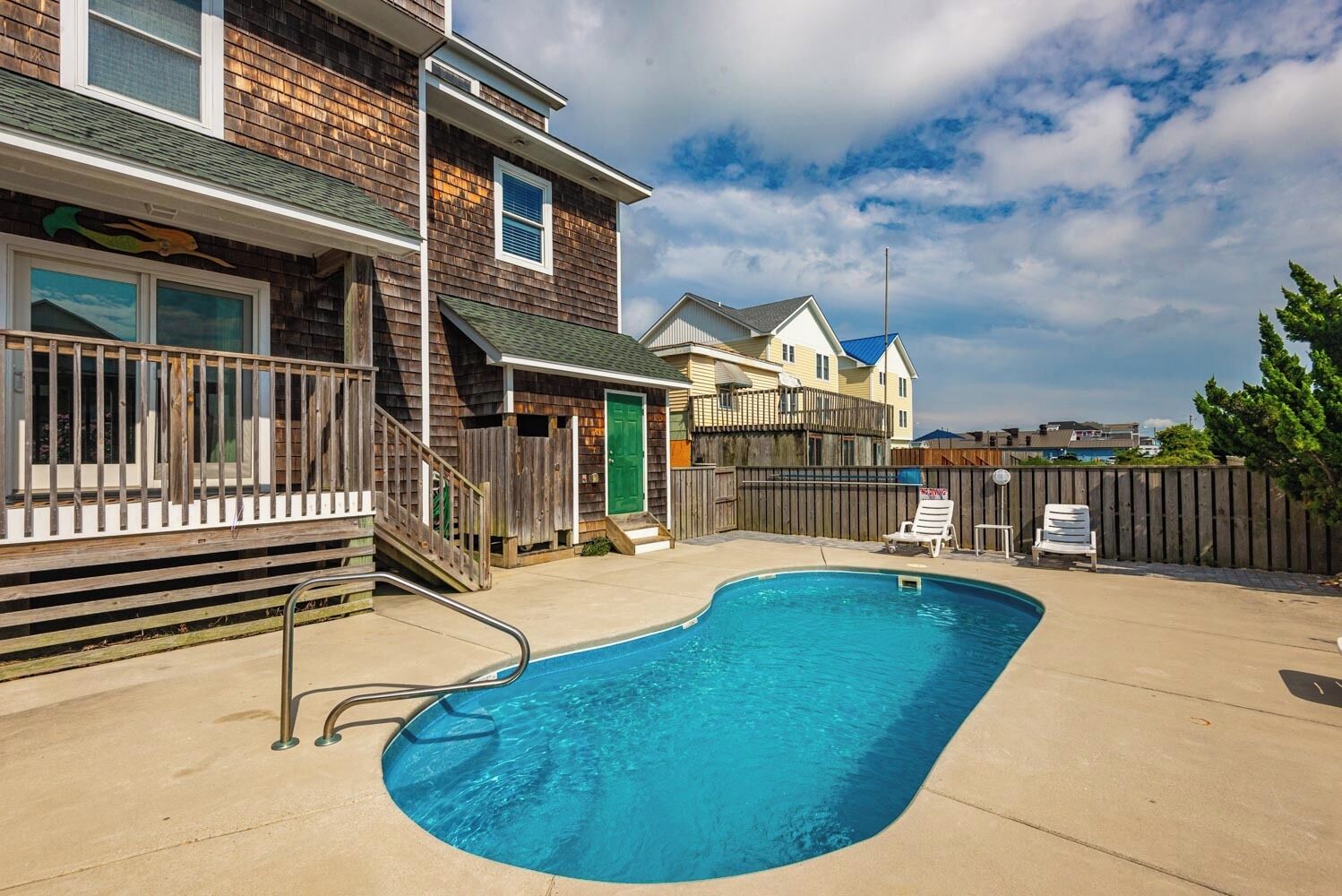 A backyard with a swimming pool, wooden deck, and a fenced area.