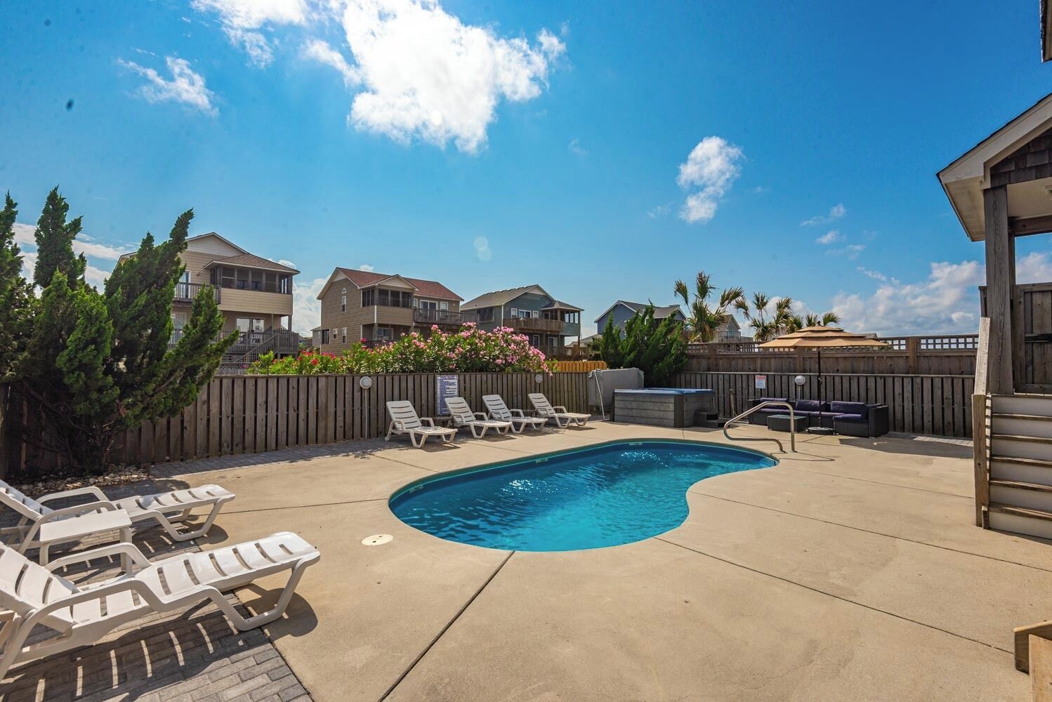 A swimming pool with lounge chairs, a wooden deck, and a wooden fence.