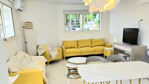 A modern living room with a yellow sofa, a dining table with chairs, and a TV. - Souplex villa Nice Fabron exclusive pool sea view, 3 min beach, streetcar, shops (Nice)