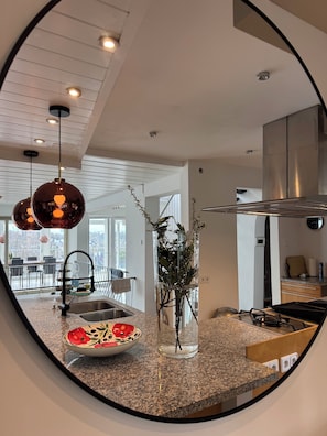 A kitchen with a granite countertop, a stainless steel sink, a vase with greenery, and pendant lighting.