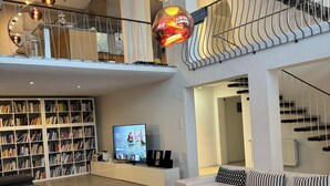 Amplia sala de estar con una gran estantería, un televisor, una mesa de centro de vidrio y una escalera moderna.