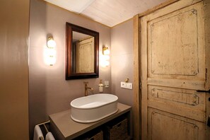 Ein Badezimmer mit einem weißen Waschbecken, einer Holztür und Wandleuchten.