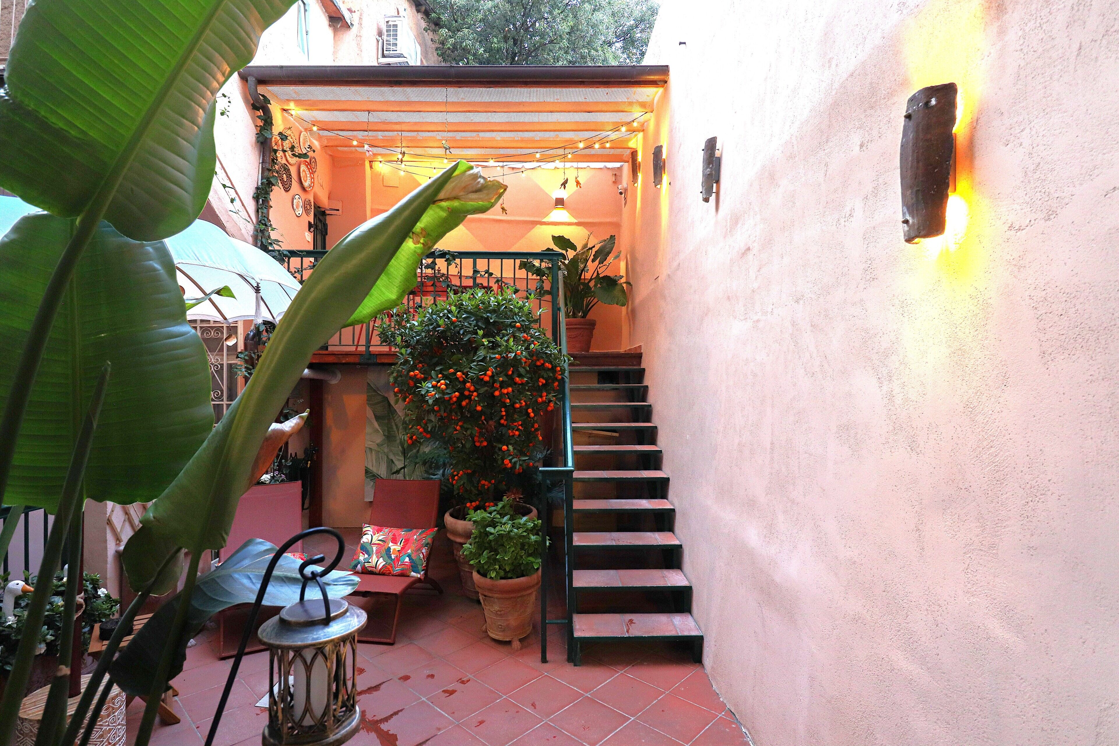 A narrow outdoor corridor with a staircase, potted plants, and a lantern.