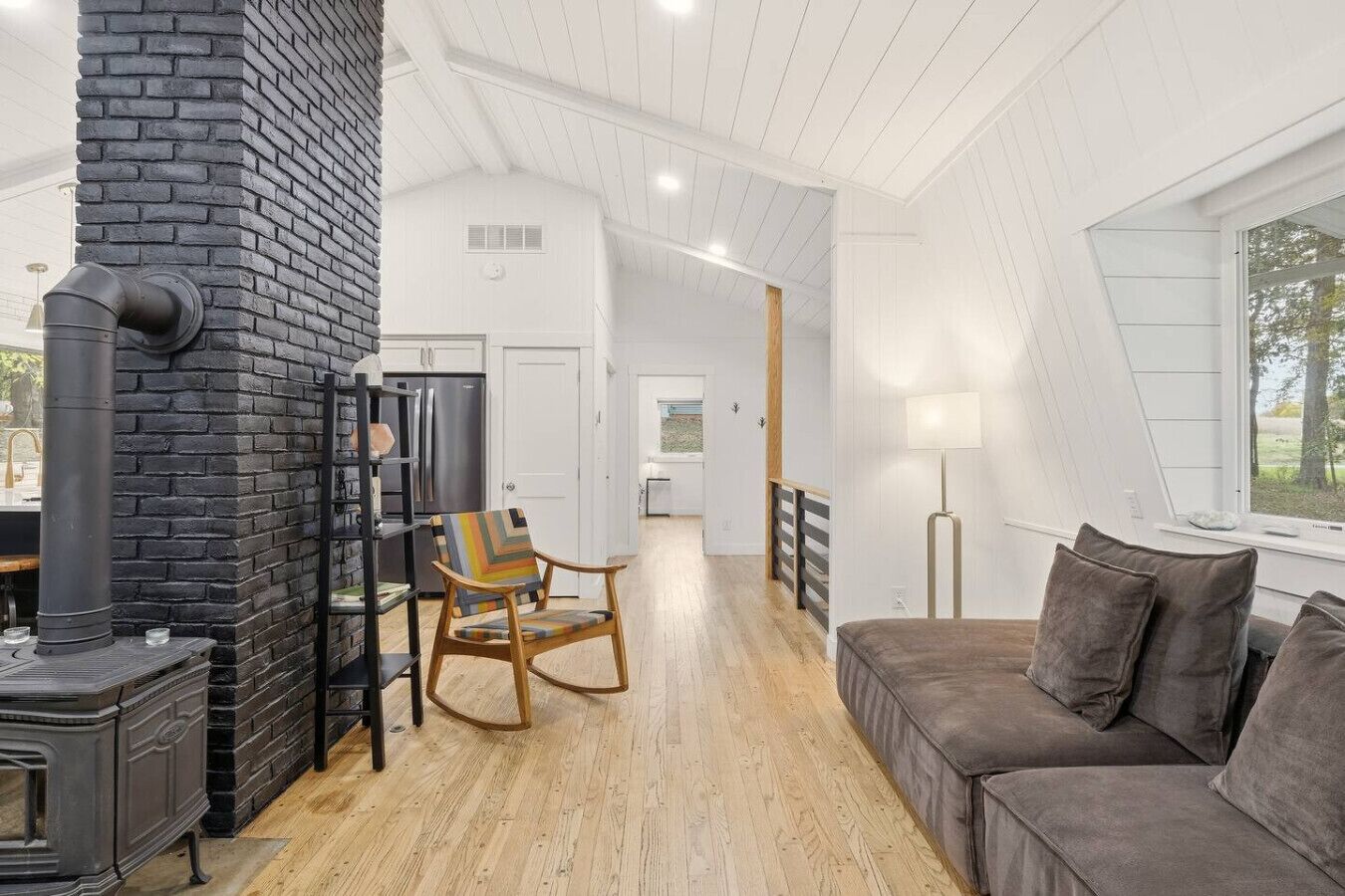 Un intérieur moderne avec une cheminée, un fauteuil à bascule en bois, un canapé et une vue par la fenêtre.