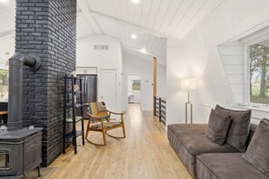 Un interior moderno con chimenea, un sillón de madera, un sofá y vistas a través de una ventana.