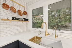 Una cocina con azulejos blancos tipo metro, un grifo dorado y una ventana con vistas a árboles.