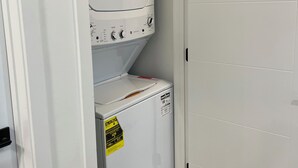Un cuarto de lavado con electrodomésticos apilados, una puerta y piso de madera.