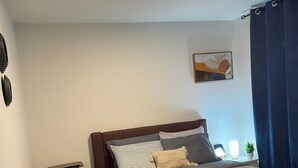 Un dormitorio con una cama, un escritorio, una silla, una planta y un cuadro en la pared.