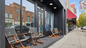Une devanture de magasin avec de grandes vitrines, un trottoir et une rangée de fauteuils à bascule à l’extérieur.