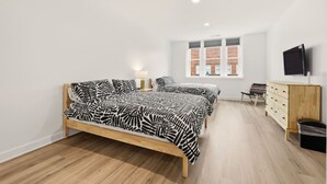 Une chambre avec deux lits, une commode en bois, une télévision et une fenêtre donnant sur un mur de briques.
