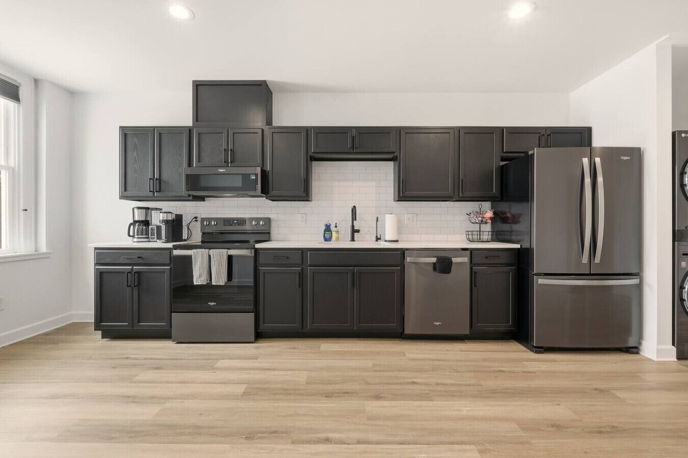 A modern kitchen with dark cabinetry, a stainless steel refrigerator, and a built-in oven.