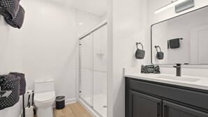 Une salle de bain moderne avec une douche à parois de verre, des toilettes blanches et un meuble-lavabo doté d’un grand miroir.