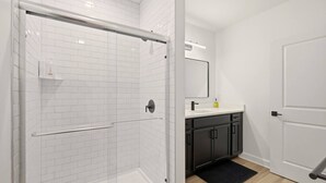 A modern bathroom with a glass-enclosed shower, white tiled walls, a black countertop, and dark cabinets.
