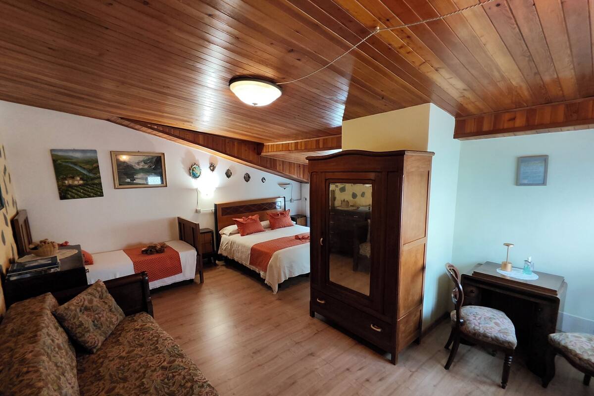 Quarto com teto de madeira, duas camas, um sofá, uma escrivaninha e um espelho.