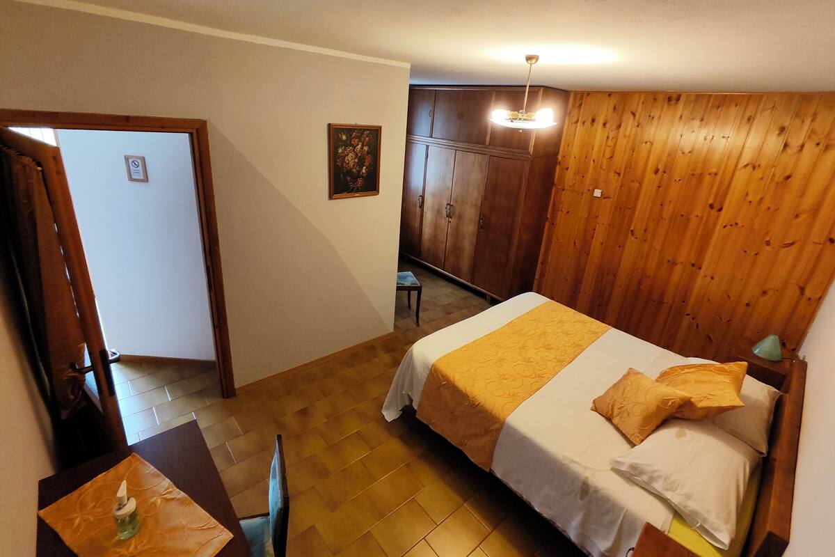 Quarto com cama, escrivaninha com cadeira, guarda-roupa e porta para outro cômodo.