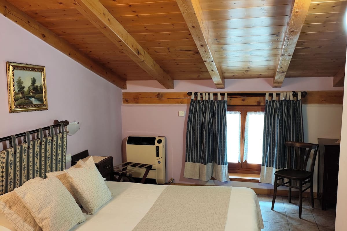 Quarto com cama, escrivaninha, cadeira, radiador e janela com cortinas.