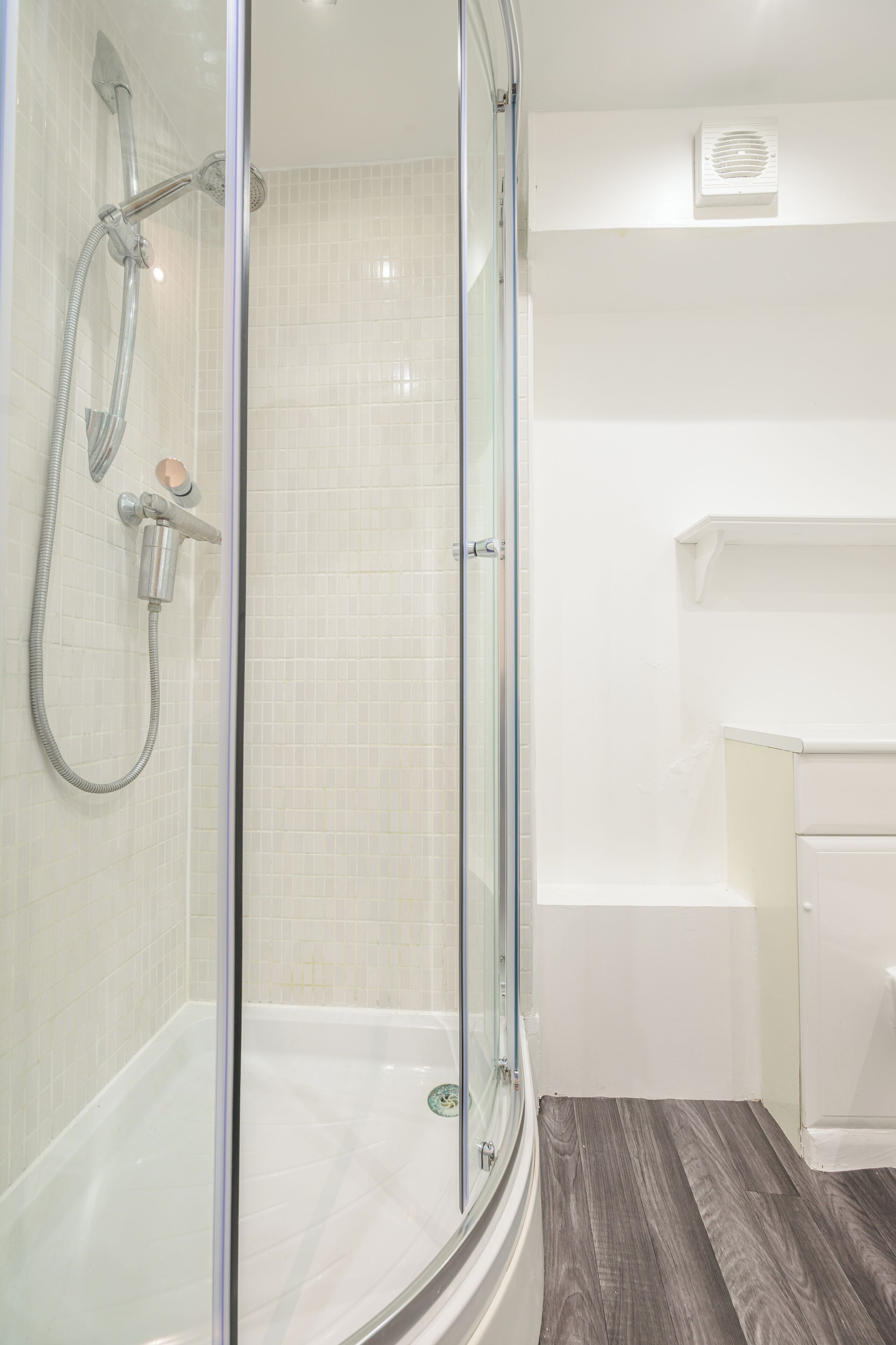 Un baño moderno con ducha acristalada, bañera blanca y piso de madera.