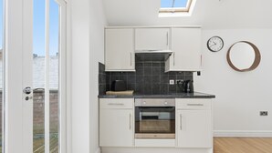 Een moderne keuken met witte kasten, een ingebouwde oven, een zwart aanrecht en een dakraam erboven.