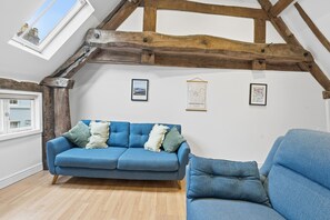 Une pièce avec un canapé bleu, des poutres en bois, une lucarne et des cartes encadrées accrochées au mur.