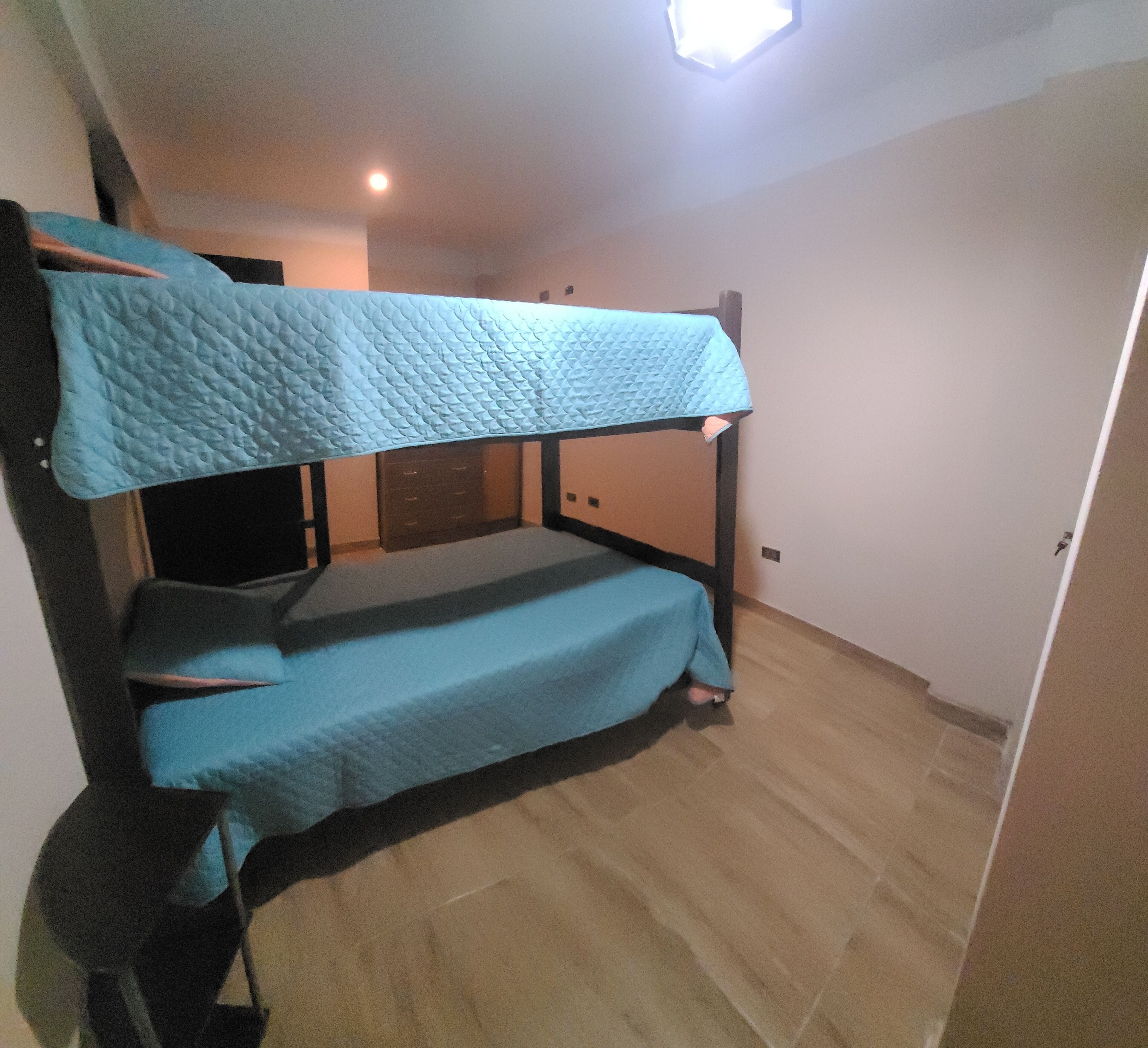 A bunk bed with a quilted top and a lower bed. There is a wooden wardrobe and a door in the room.