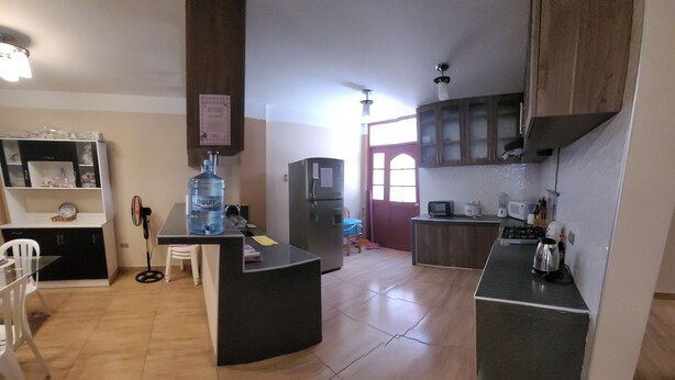 A kitchen with a refrigerator, microwave, and water dispenser. There is a dining table with chairs. - Giovi's House (Moquegua)