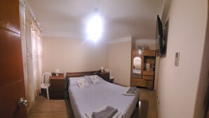 A hotel room with a bed, a desk, a chair, a wardrobe, and a television. - Giovi's House (Moquegua)