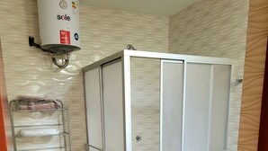 A bathroom with a toilet, a shower enclosure, a metal shelf with towels, and a water heater. - Giovi's House (Moquegua)