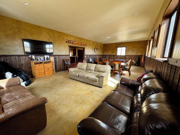 A spacious living room with a large sofa, a dining table with chairs, a wooden cabinet, and a mounted television.
