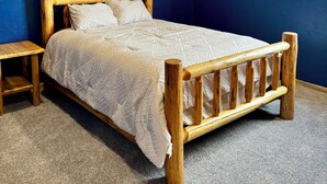 Un dormitorio con una cama de madera, un ventilador de techo, un cuadro en la pared y una mesita de noche de madera.