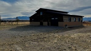 Una cabaña moderna de madera con garaje, ubicada en un campo cubierto de hierba con montañas al fondo.