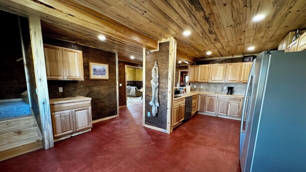 Una cocina con armarios de madera, un refrigerador y un comedor con una silla.