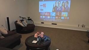 Ein Wohnzimmer mit einer Couch, einem Couchtisch mit Blumen und einer Projektionsleinwand, die einen Film zeigt.