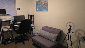 Ein Zimmer mit Schreibtisch, Computer, Stuhl, Sofa und einem Ringlicht.