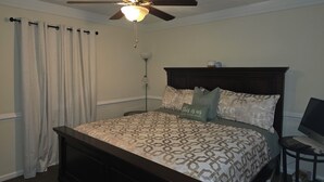 Ein Schlafzimmer mit einem Bett, einem Deckenventilator, einem Nachttisch und einer Lampe.
