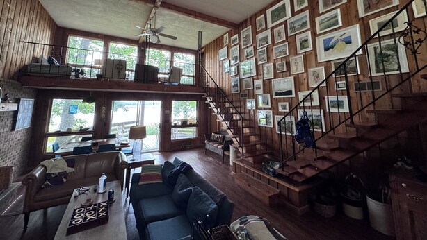 A spacious living area with a high ceiling, wooden walls, a staircase with a railing, and a wall adorned with framed pictures.