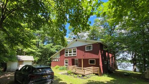 A red cabin with a dock, a car parked in front, and a small shed nearby.
