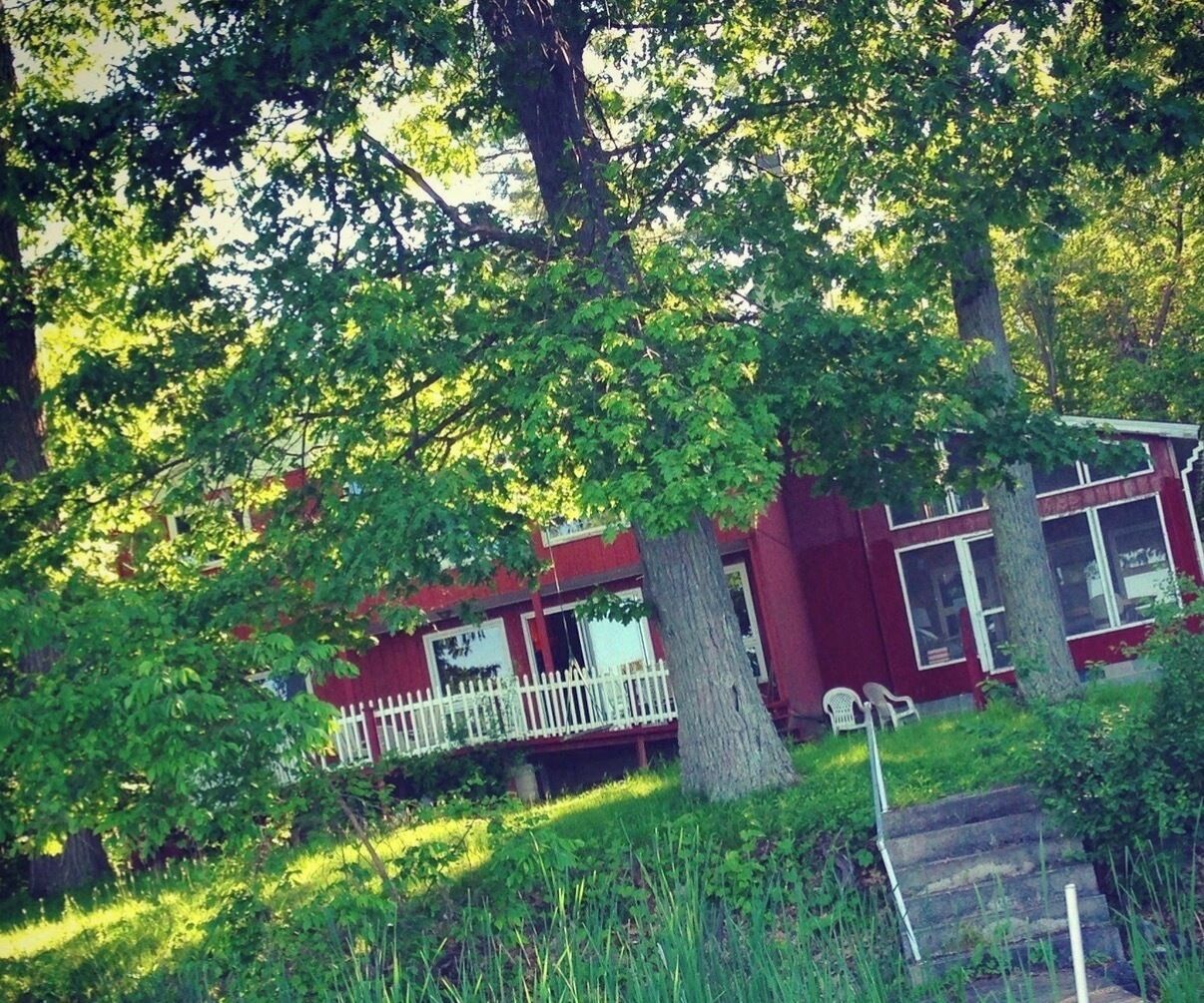 Un bâtiment rouge avec un porche blanc, entouré d’arbres.