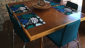 A dining area with a wooden table, blue chairs, a hanging light fixture, and a brick wall.