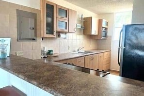 A kitchen with wooden cabinets, a stainless steel refrigerator, and a granite countertop.