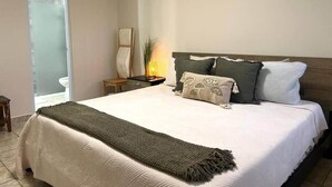 Een slaapkamer met een bed, nachtkastjes, een lamp en uitzicht op een badkamer.