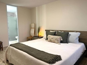 Een slaapkamer met een bed, nachtkastjes, een lamp en uitzicht op een badkamer.