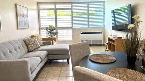 Een woonkamer met een modulaire bank, een eettafel met placemats, een flatscreen televisie en een potplant.